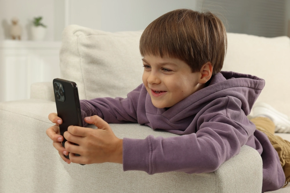 Un niño pequeño sonriente utilizando un smartphone, ilustrando el uso temprano de teléfonos inteligentes en la infancia