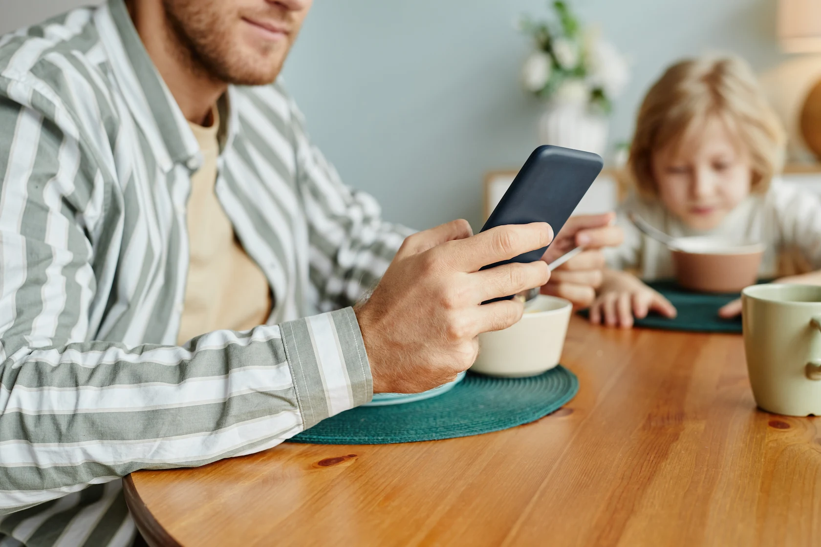 Padre revisando el celular junto a su hijo durante el desayuno, uso responsable del WhatsApp de apoderados